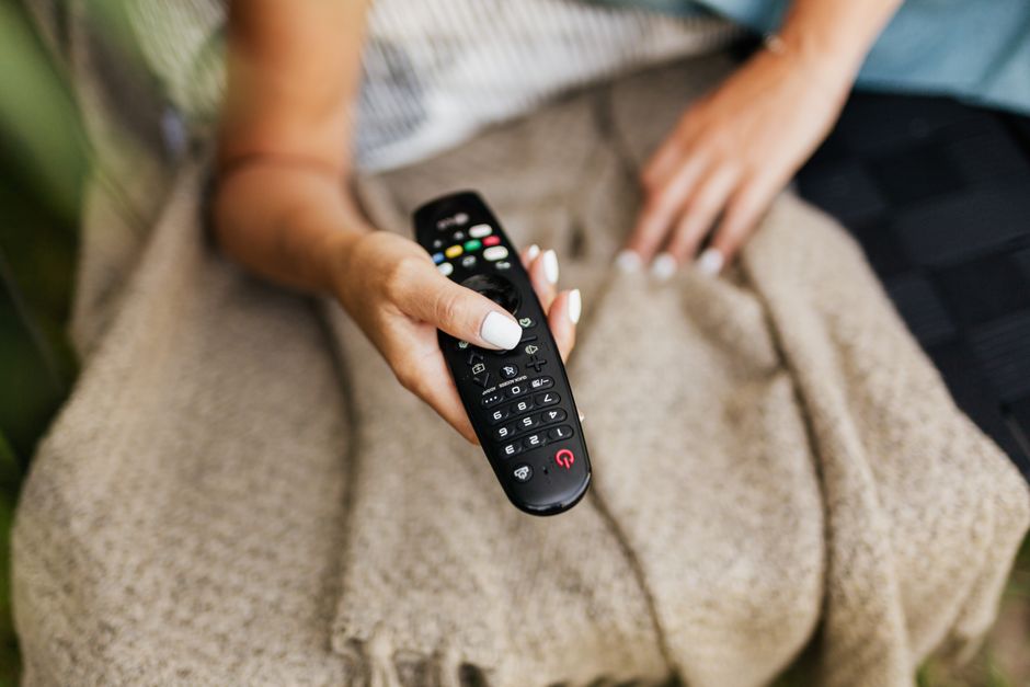 Hand holding a television remote in front of a screen